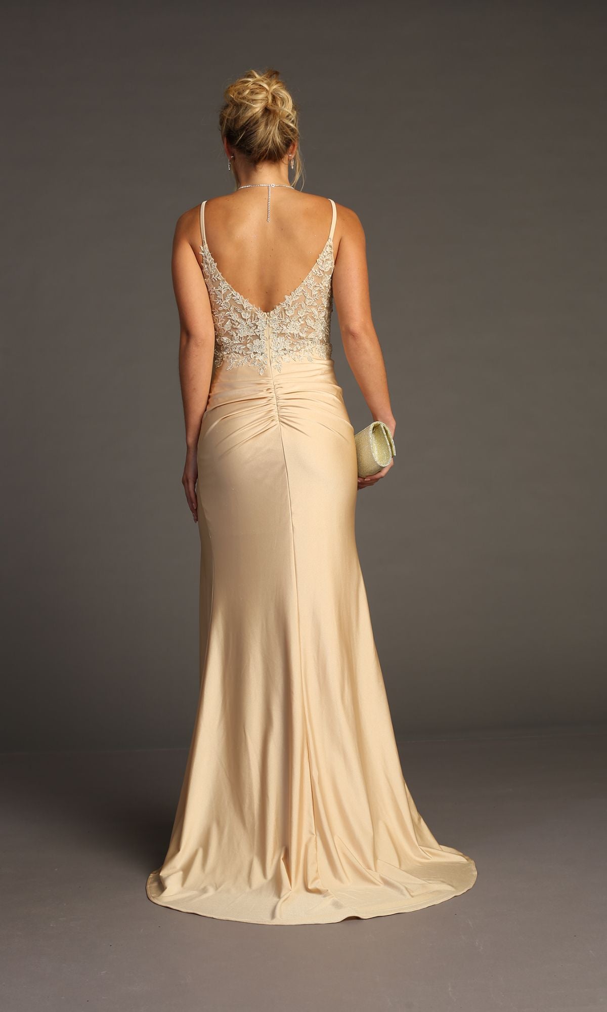 A woman in the Chicas YG5033 Lace-Bodice Slinky Long Prom Dress, featuring beige embroidered lace and a low back, stands facing away while holding a small clutch.
